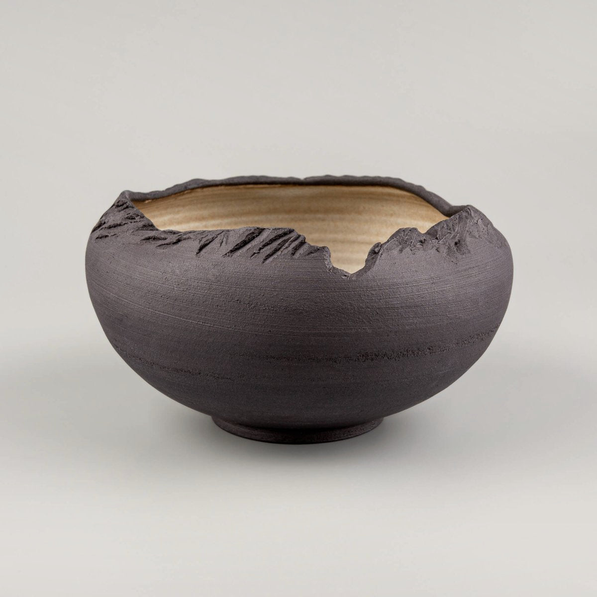 Side view of handmade stoneware bowl with carved raw black exterior and sculptural open rim.