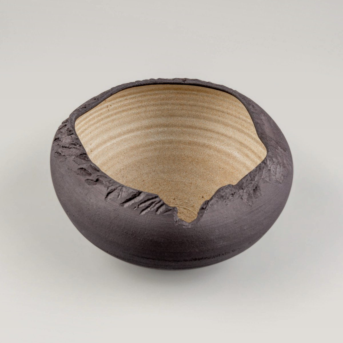 Angled front view of black stoneware bowl with natural textured surface and glazed interior.