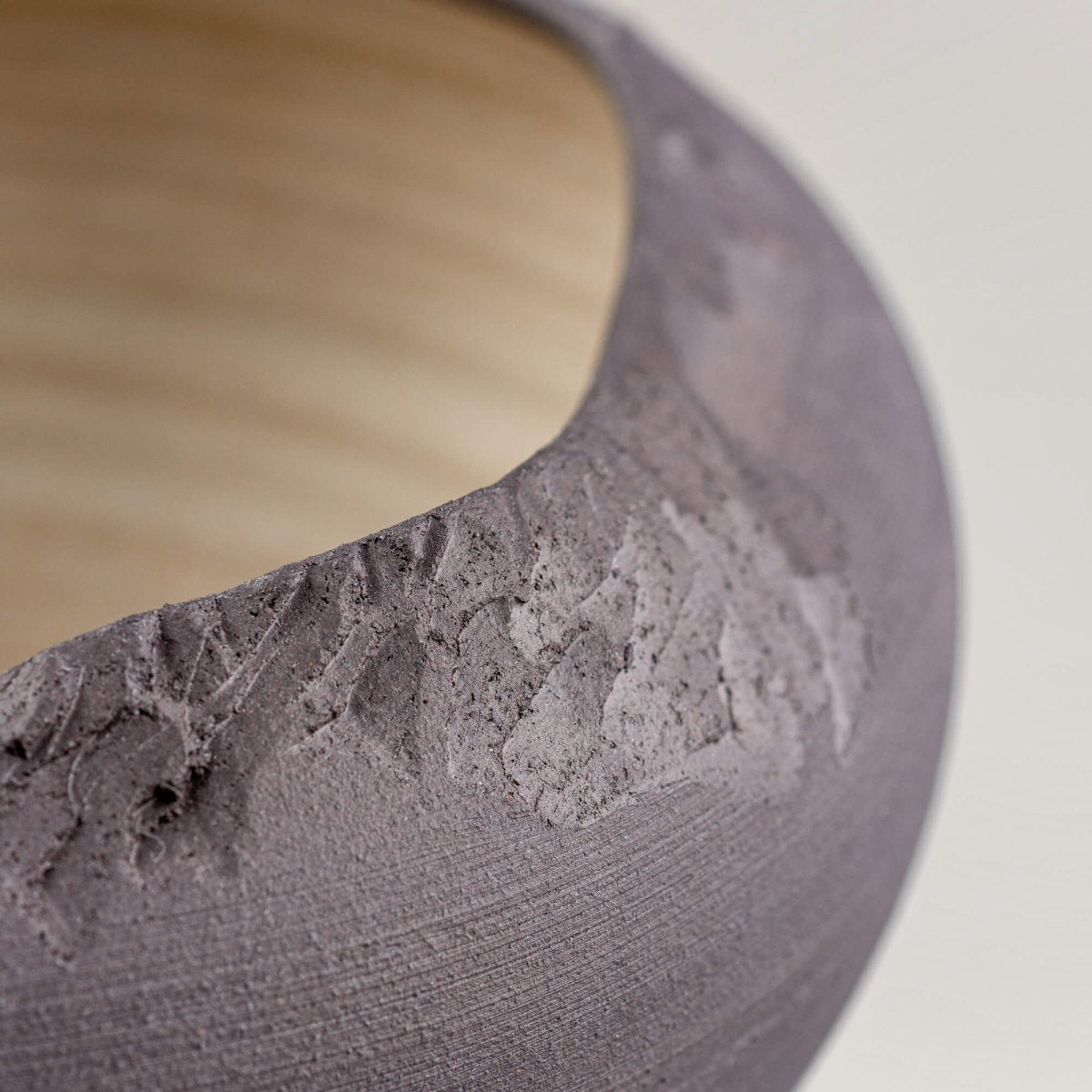 Macro detail of carved edge and matte black stoneware finish on artisan bowl.