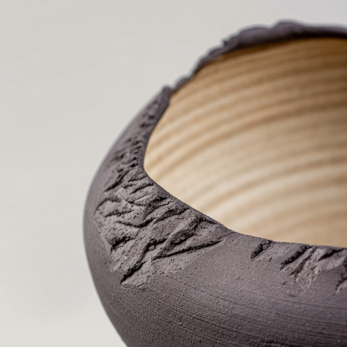 Side angle showcasing rough rim detail and dark stoneware texture on artisan-crafted bowl.