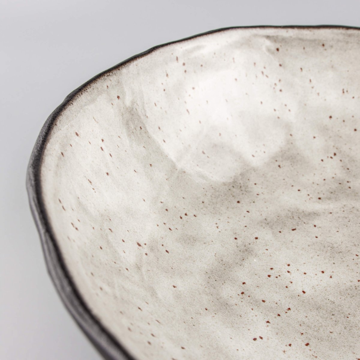 Curved rim section of artisan ceramic bowl showing tactile texture and hand-shaped edge.