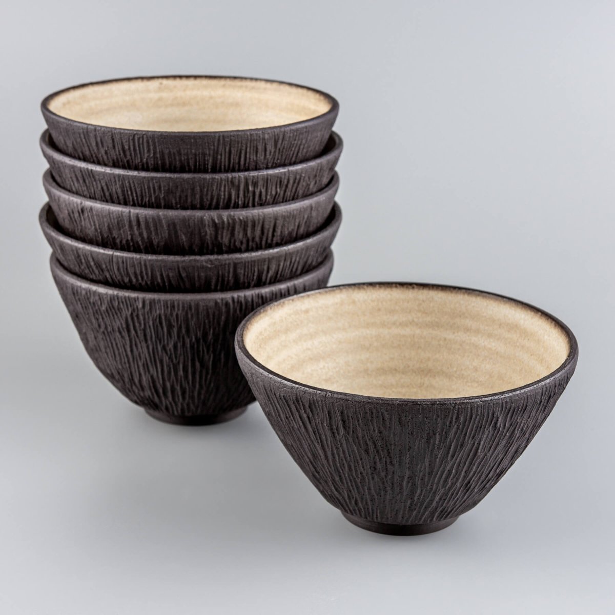 Stack of handcrafted dark stoneware bowls with contrasting light interior glaze.