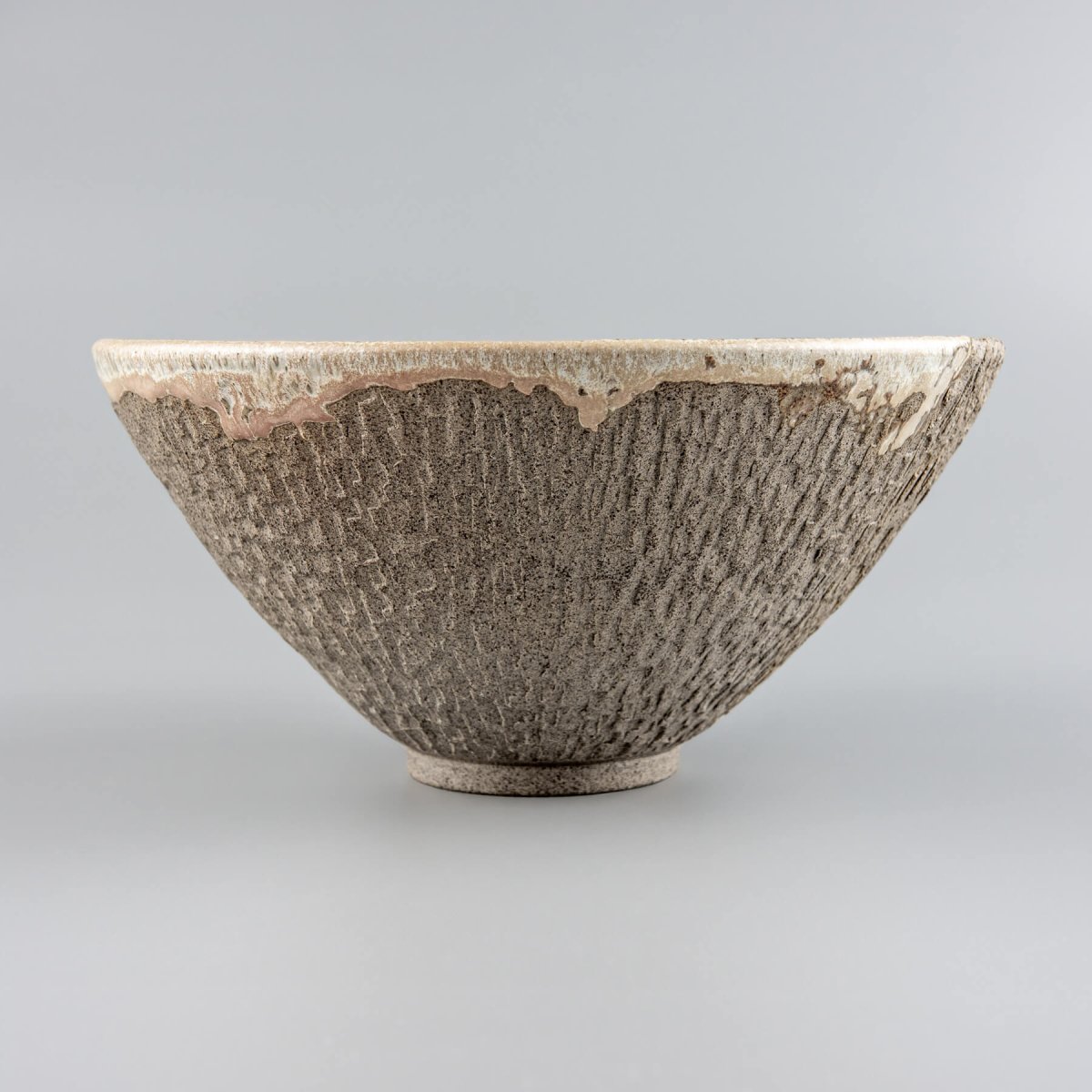 Decorative ceramic vessel with dual finish—glazed interior and unglazed hand-carved exterior.
