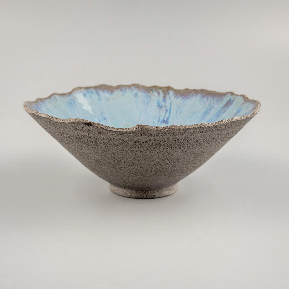 Angled view of handmade stoneware bowl with flared edges and light blue glazed interior.