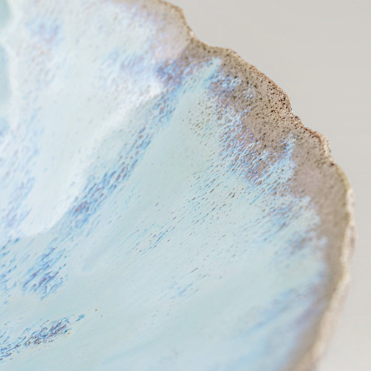 Close-up of textured rim on stoneware bowl with layered glaze in soft blue tones.