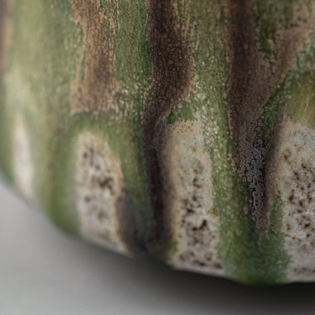 Handcrafted ceramic mug detail with layered green and brown glaze, showing fine texture and artisanal finish.