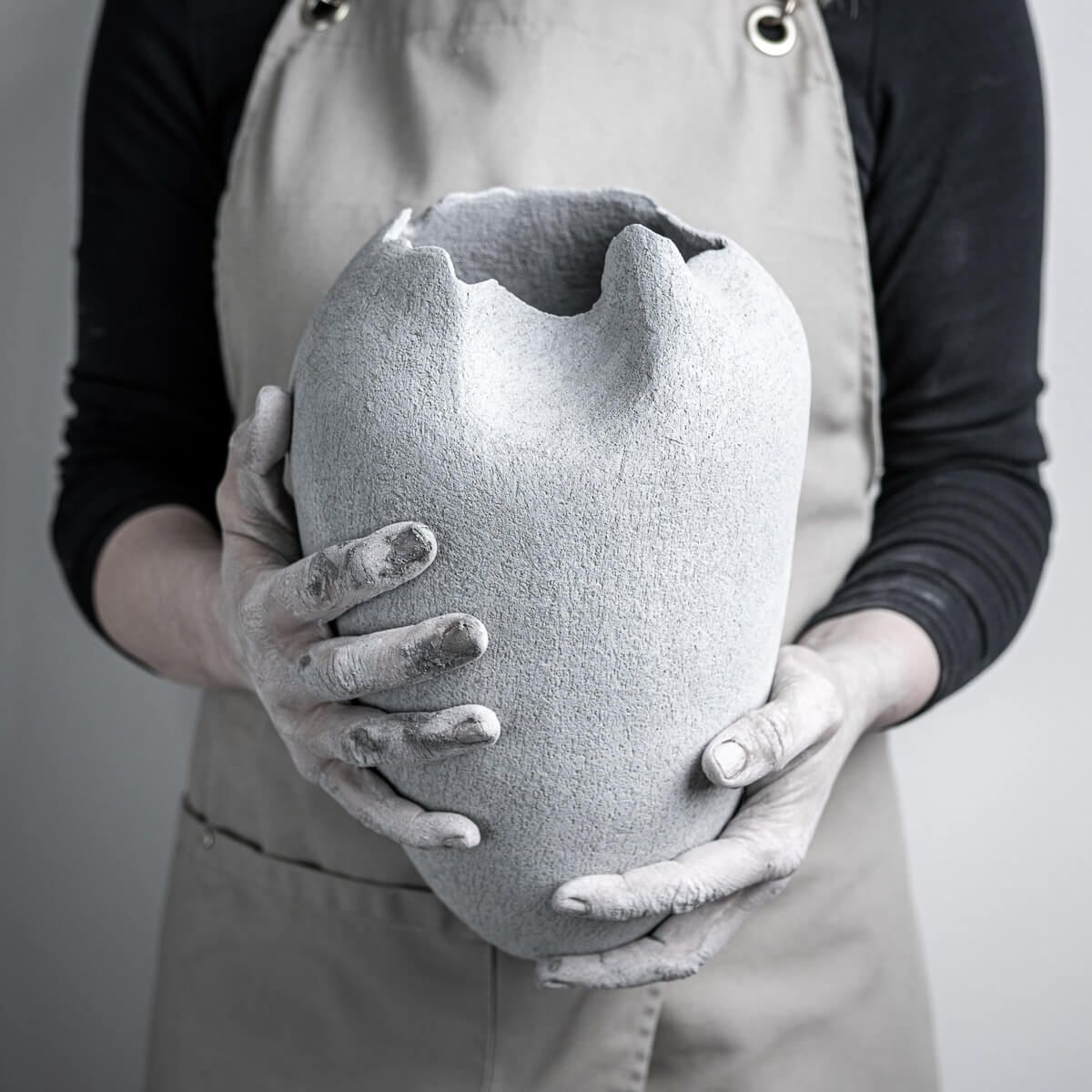 Hands holding a handmade pottery vase in stoneware clay, luxury collectible pottery for boutique hotel and interior design.