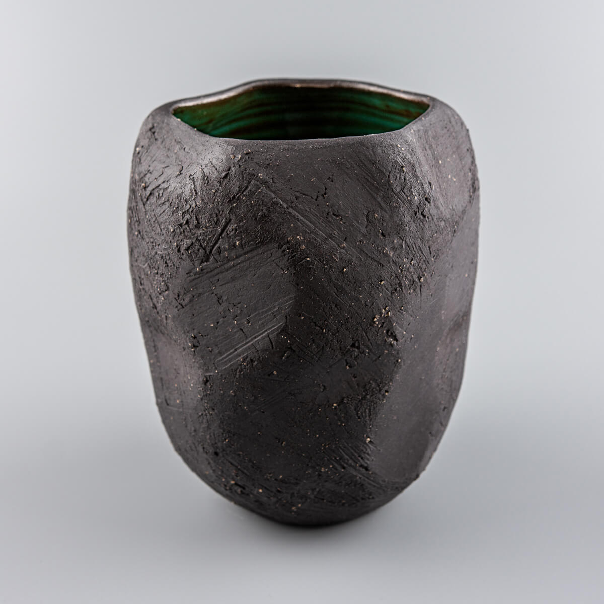 Handmade pottery vase with black stoneware texture and green glazed interior.