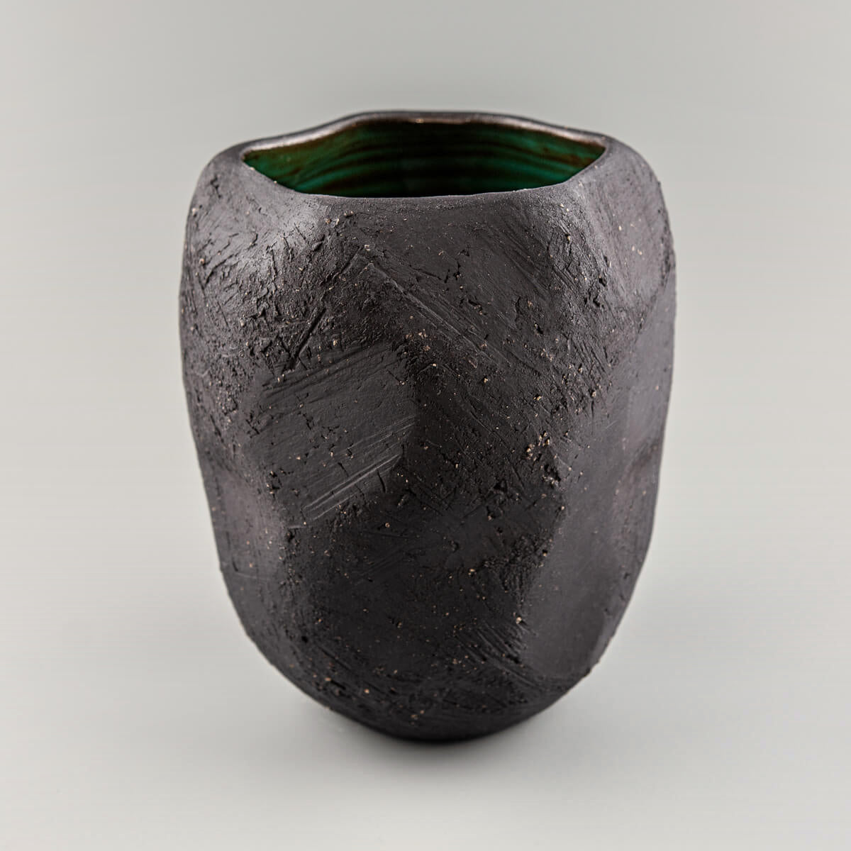 Handmade pottery vase with black stoneware texture and green glazed interior.