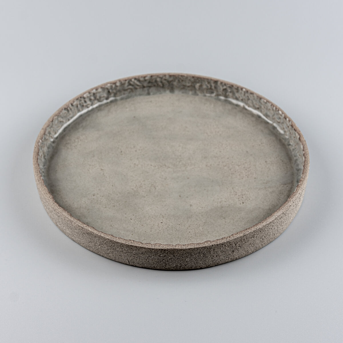 Top view of round ceramic plate with subtle carved detail and glossy artisanal finish.