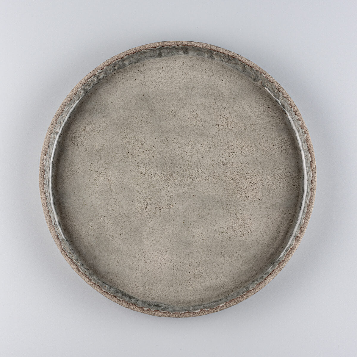 Stoneware dinner plate with semi-transparent glossy gray glaze and handcrafted carved inner edge.