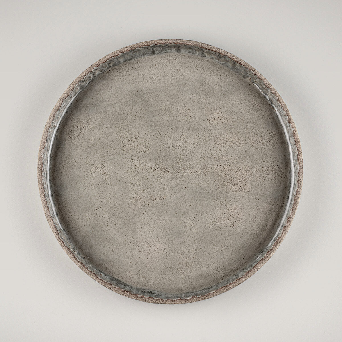 Stoneware dinner plate with semi-transparent glossy gray glaze and handcrafted carved inner edge.