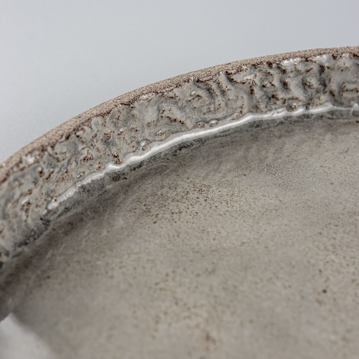 Close-up of hand-carved rim and glossy gray ceramic surface revealing clay texture.