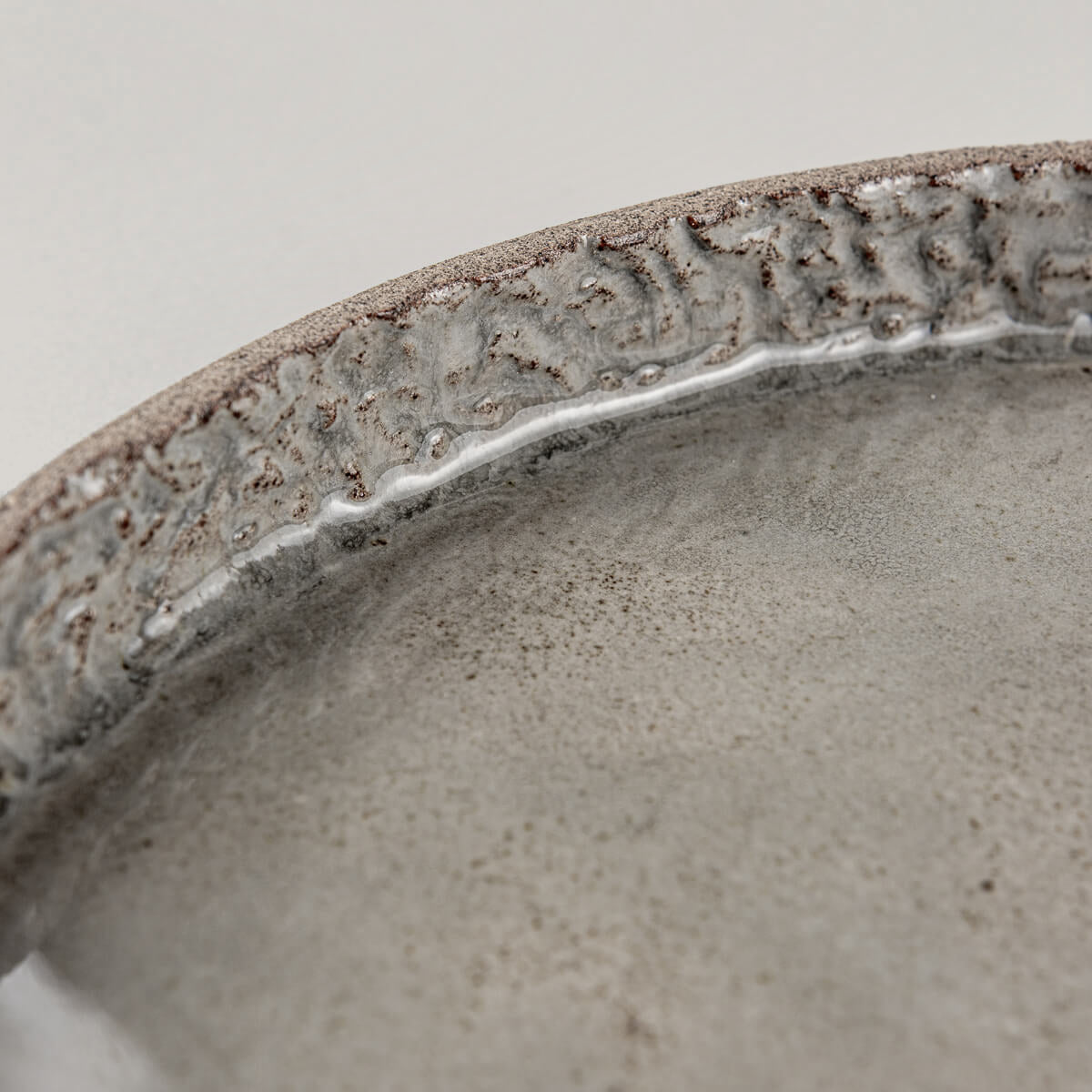 Close-up of hand-carved rim and glossy gray ceramic surface revealing clay texture.