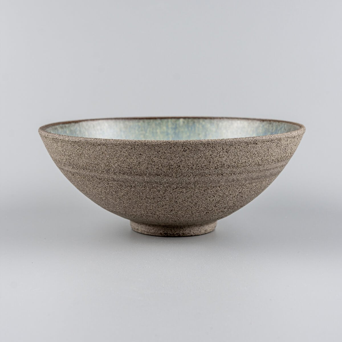 Side view of handmade ceramic bowl with raw textured exterior and flared round shape.