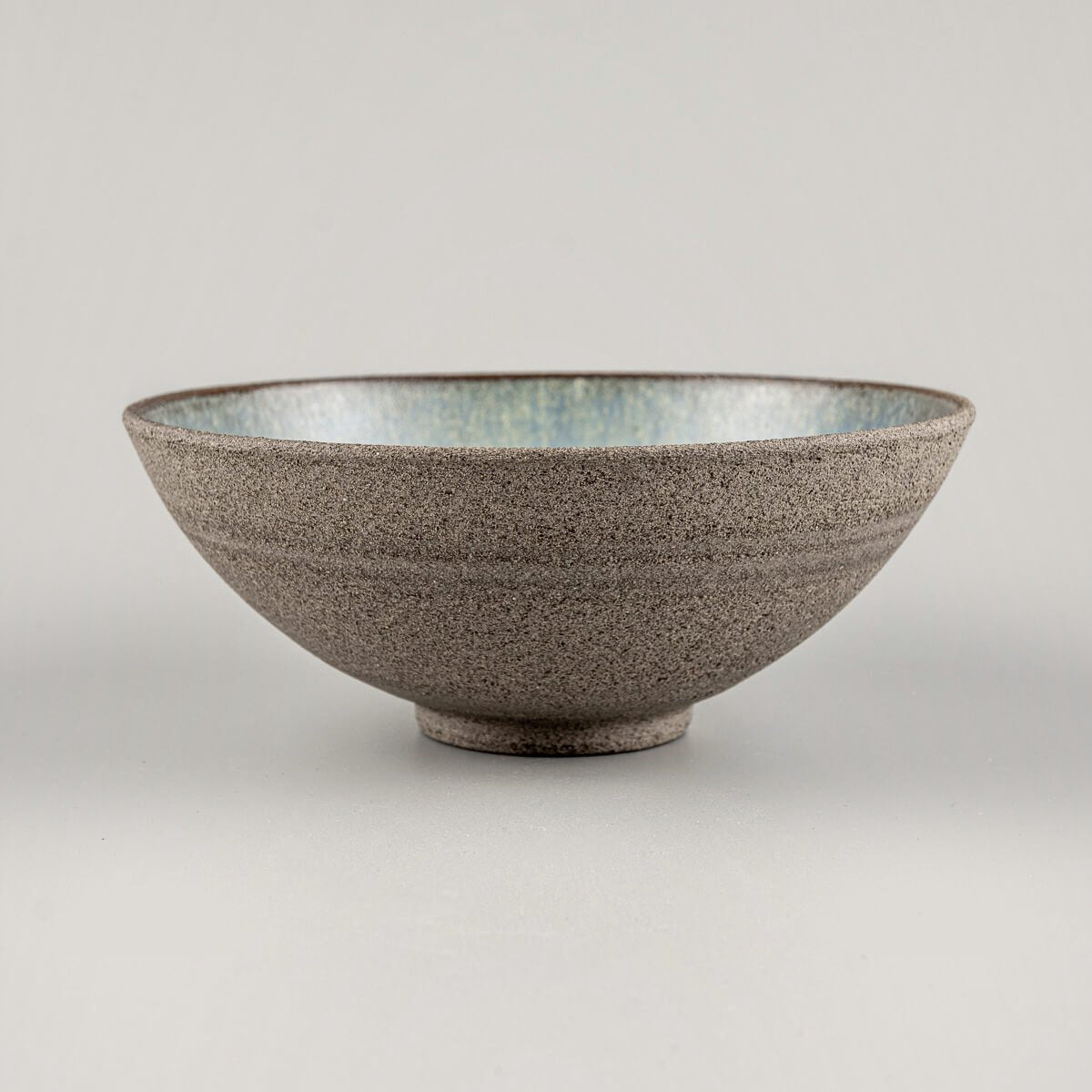 Side view of handmade ceramic bowl with raw textured exterior and flared round shape.