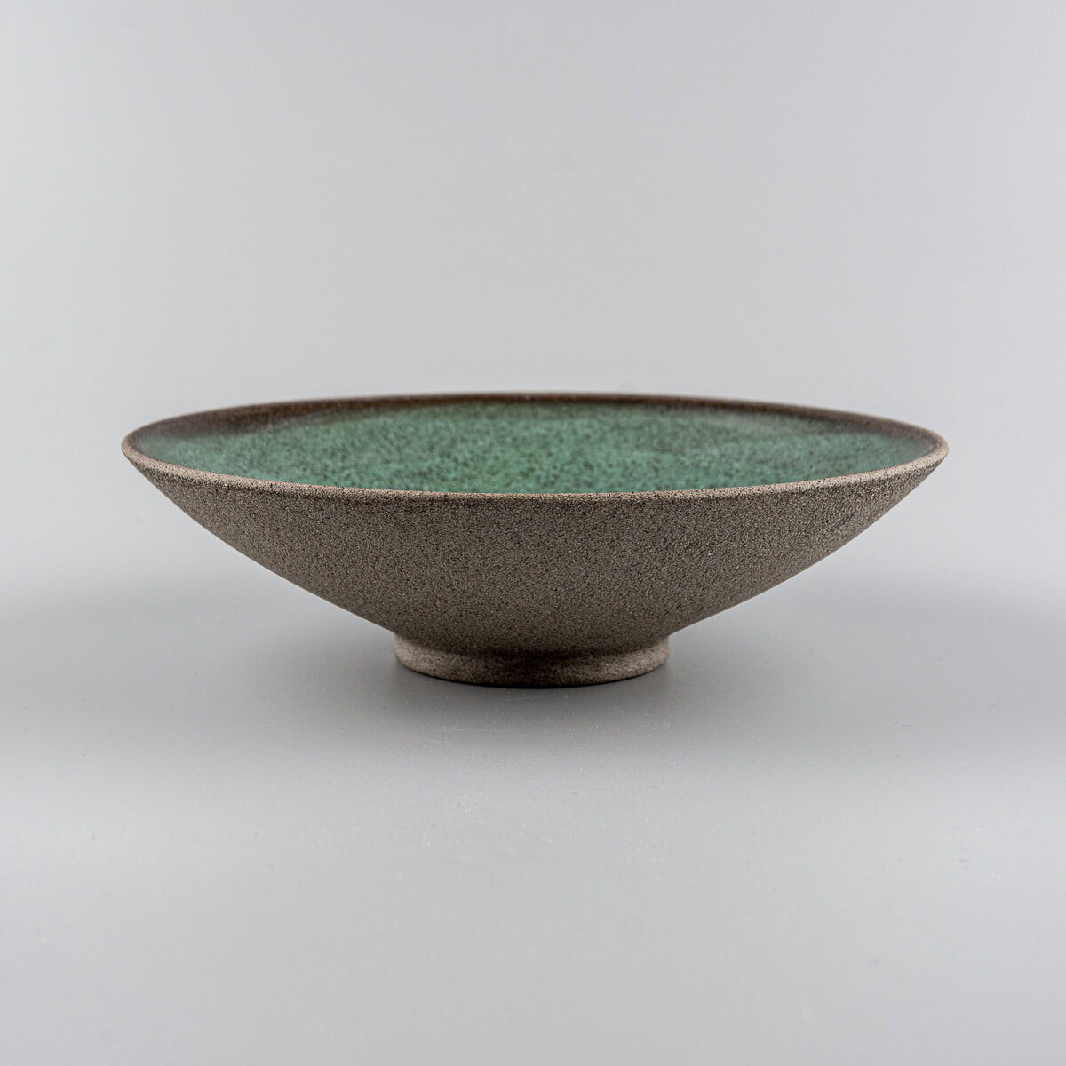 Side angle of elevated handmade stoneware dinner plate with unglazed textured exterior.
