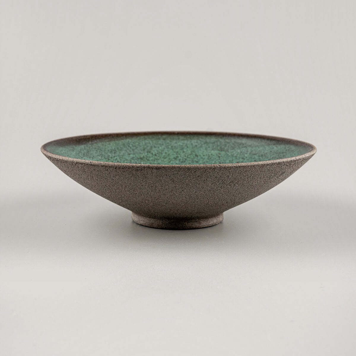 Side angle of elevated handmade stoneware dinner plate with unglazed textured exterior.