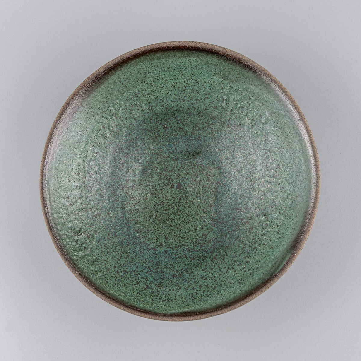 Top view of handmade stoneware plate with dark green glazed surface and raw clay edges.
