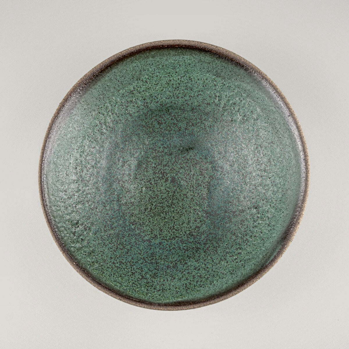 Top view of handmade stoneware plate with dark green glazed surface and raw clay edges.