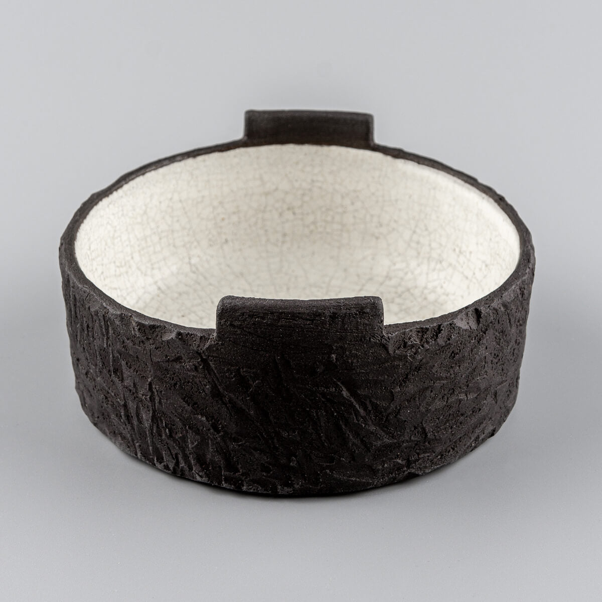 Front view of handmade pottery bowl with raw black clay exterior and matte crackled interior glaze.