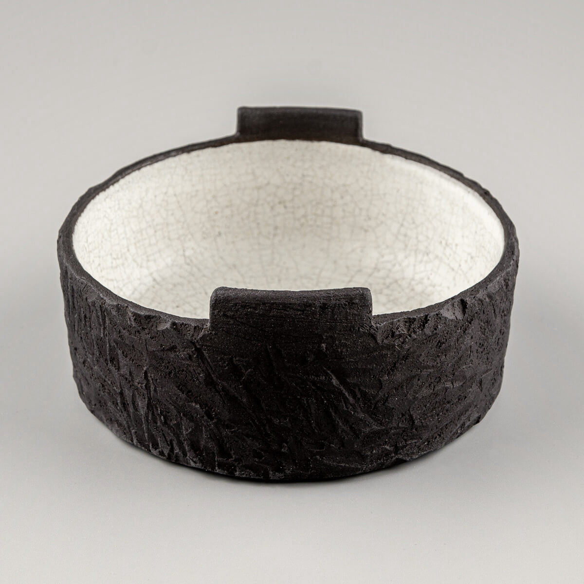 Front view of handmade pottery bowl with raw black clay exterior and matte crackled interior glaze.