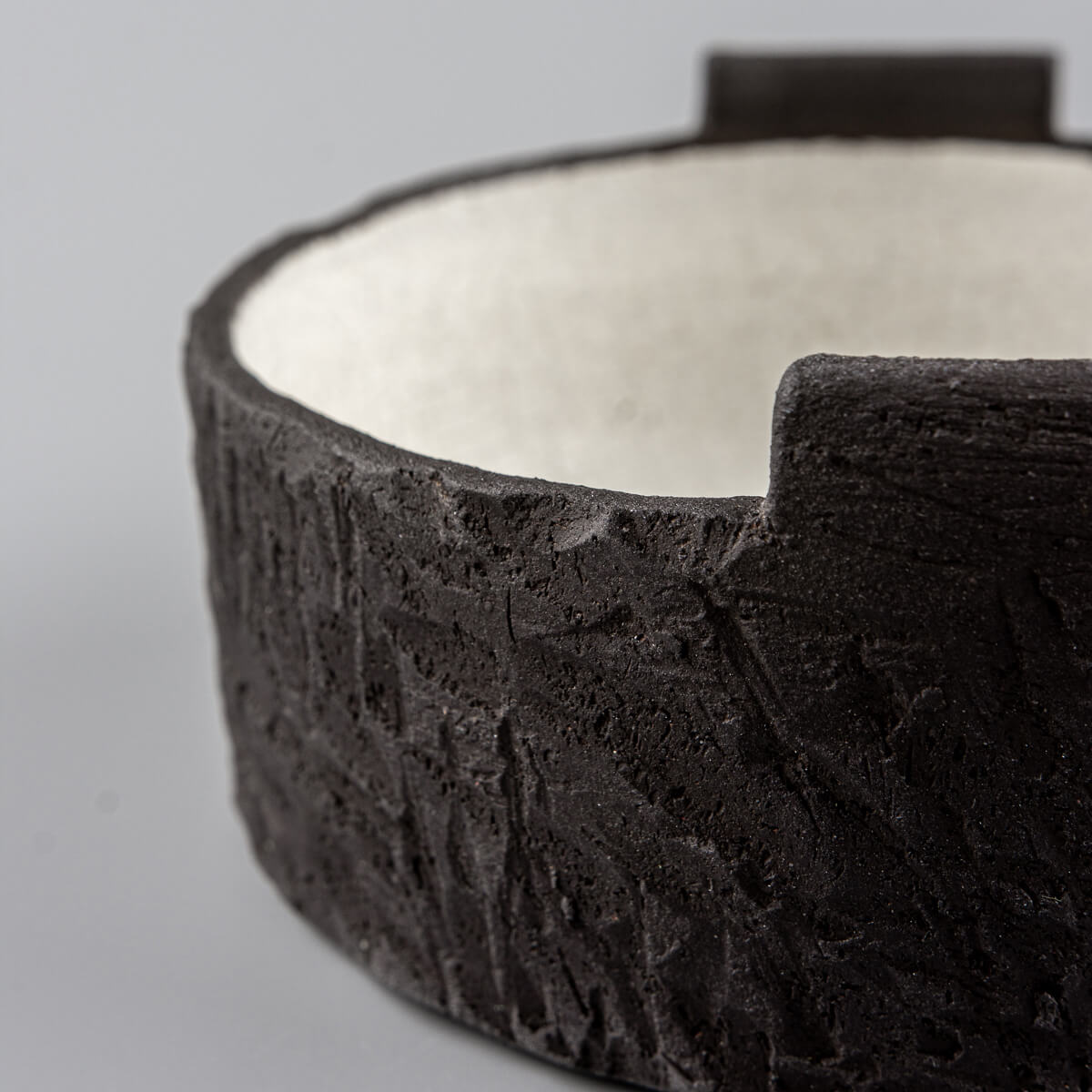 Angled side view of artisanal pottery bowl with sculptural black clay surface and raised accents.