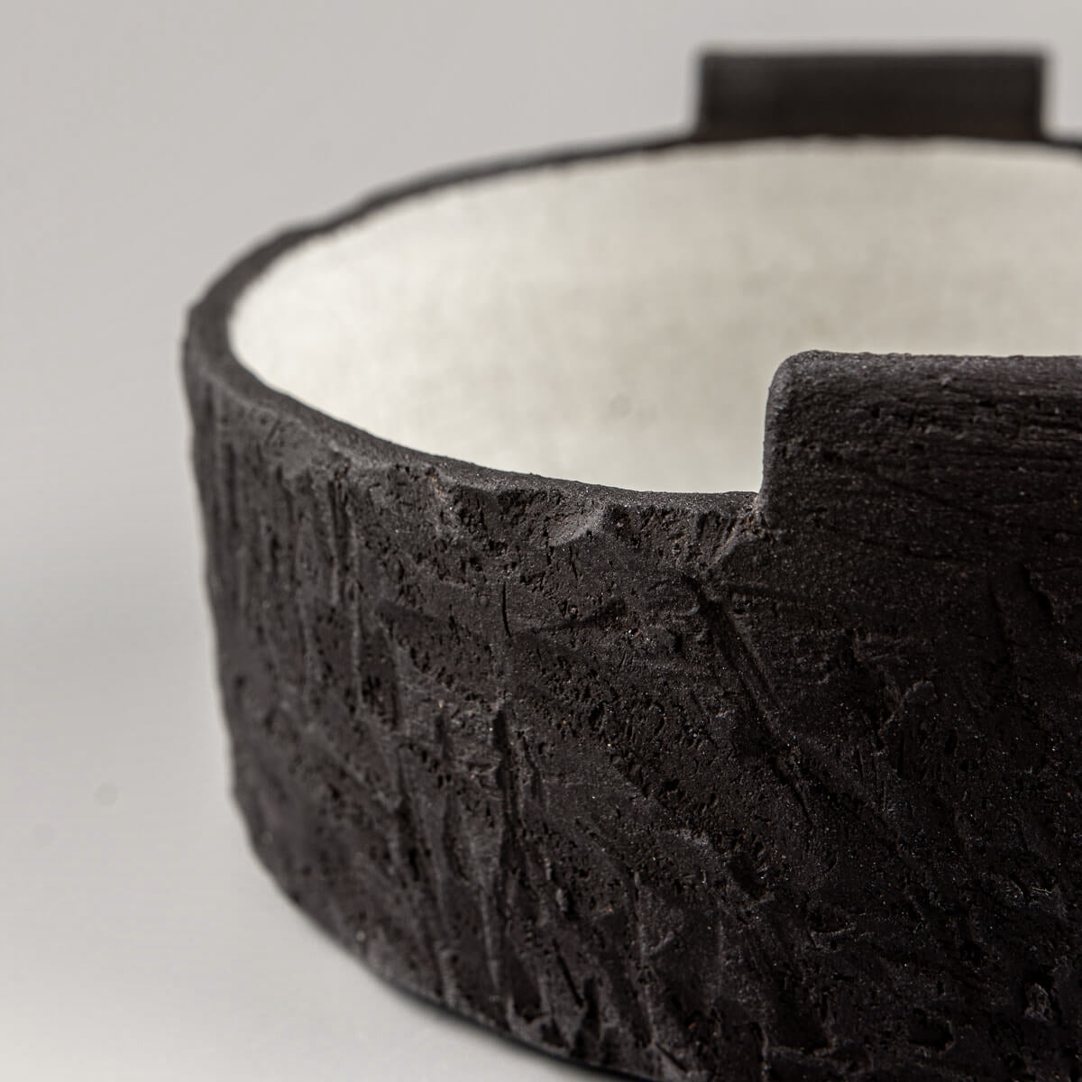Angled side view of artisanal pottery bowl with sculptural black clay surface and raised accents.