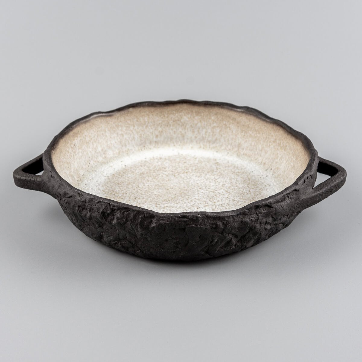 Side view of handcrafted ceramic plate with integrated handles and rugged dark clay body.