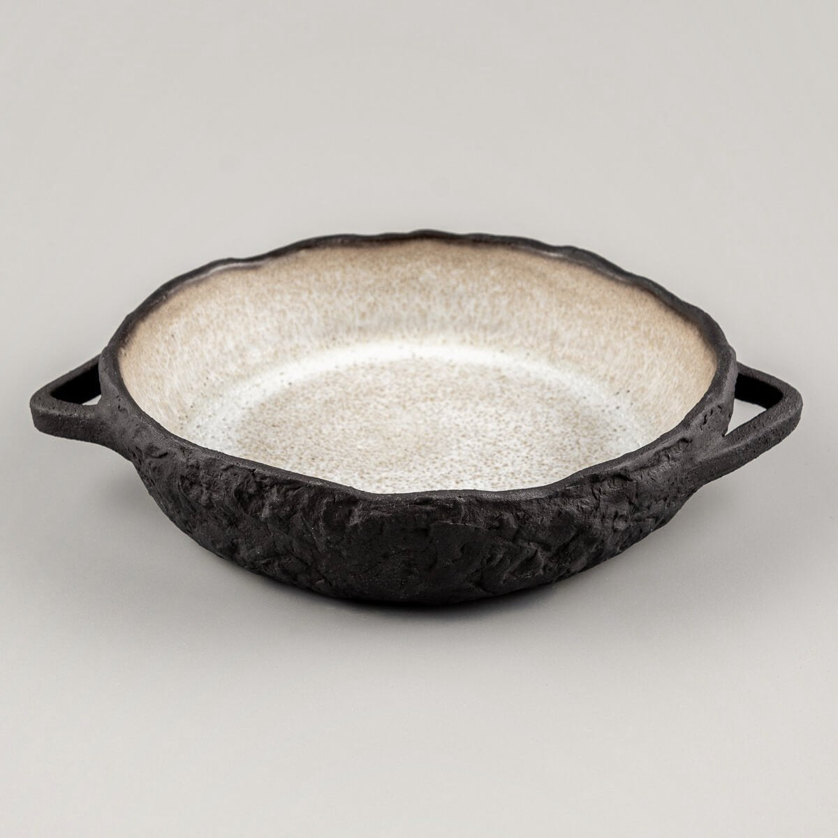 Side view of handcrafted ceramic plate with integrated handles and rugged dark clay body.