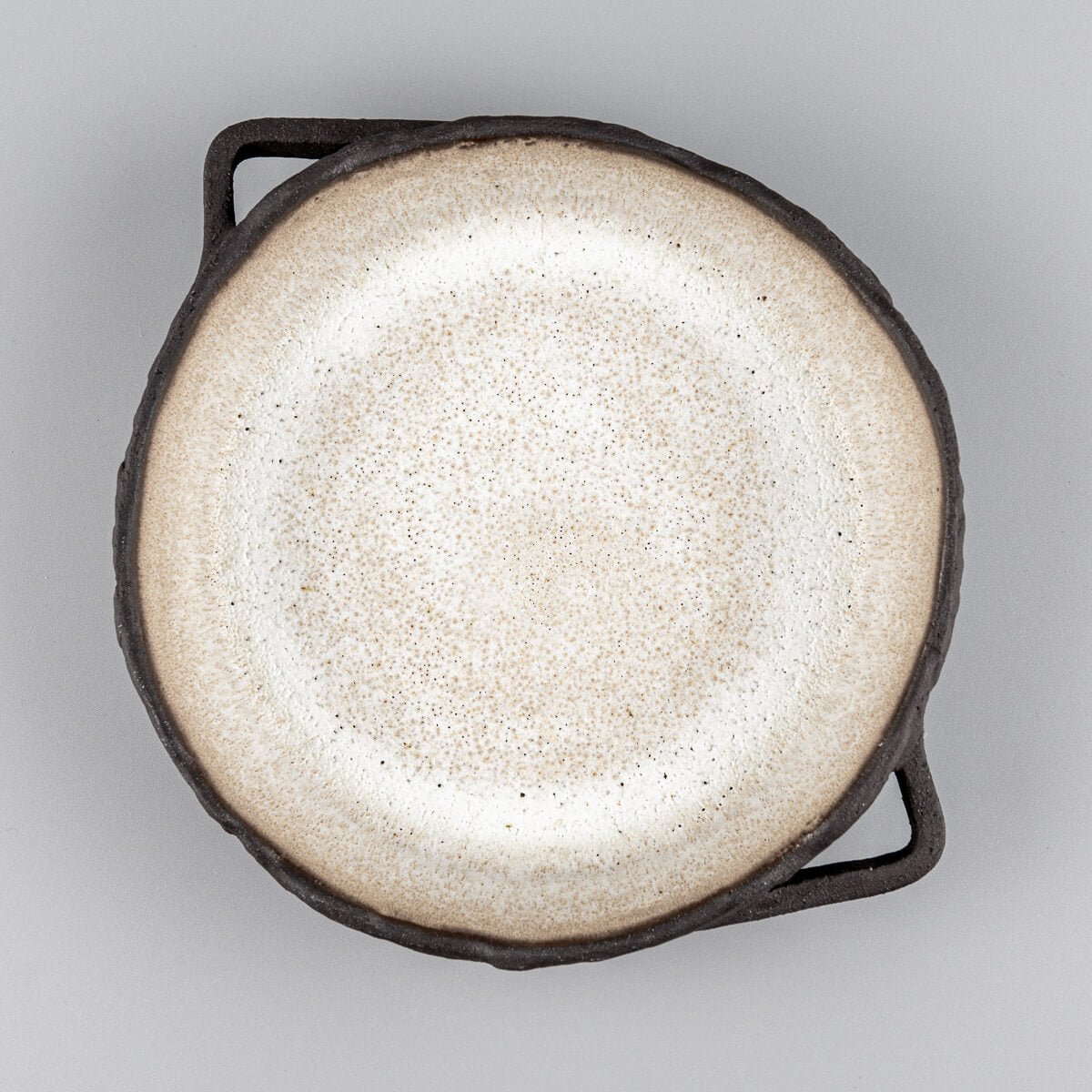Top view of artisanal ceramic plate with textured black exterior and matte glazed interior for fine dining settings.