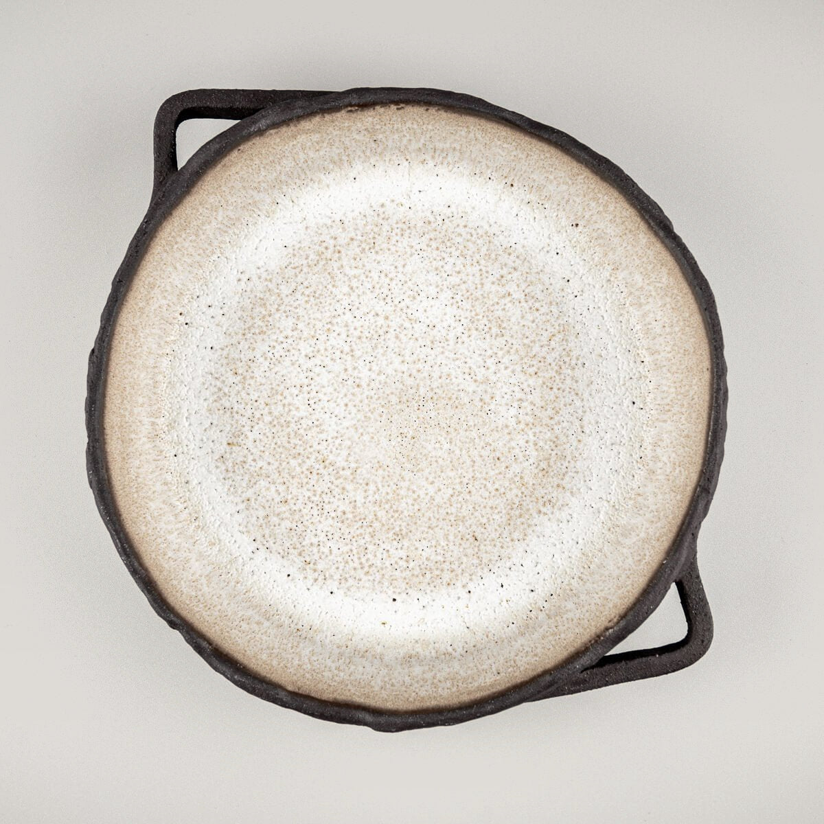 Top view of artisanal ceramic plate with textured black exterior and matte glazed interior for fine dining settings.