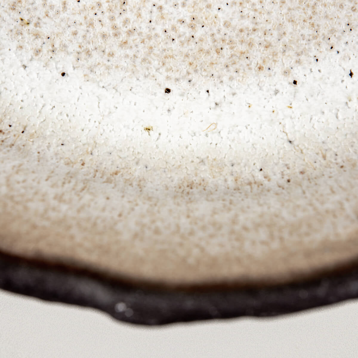 Interior surface of artisanal ceramic plate with soft speckled texture and collectible pottery appeal.