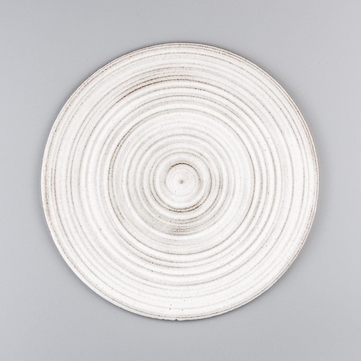 Flat handcrafted ceramic plate with matte white glaze and textured rings for fine dining restaurants.