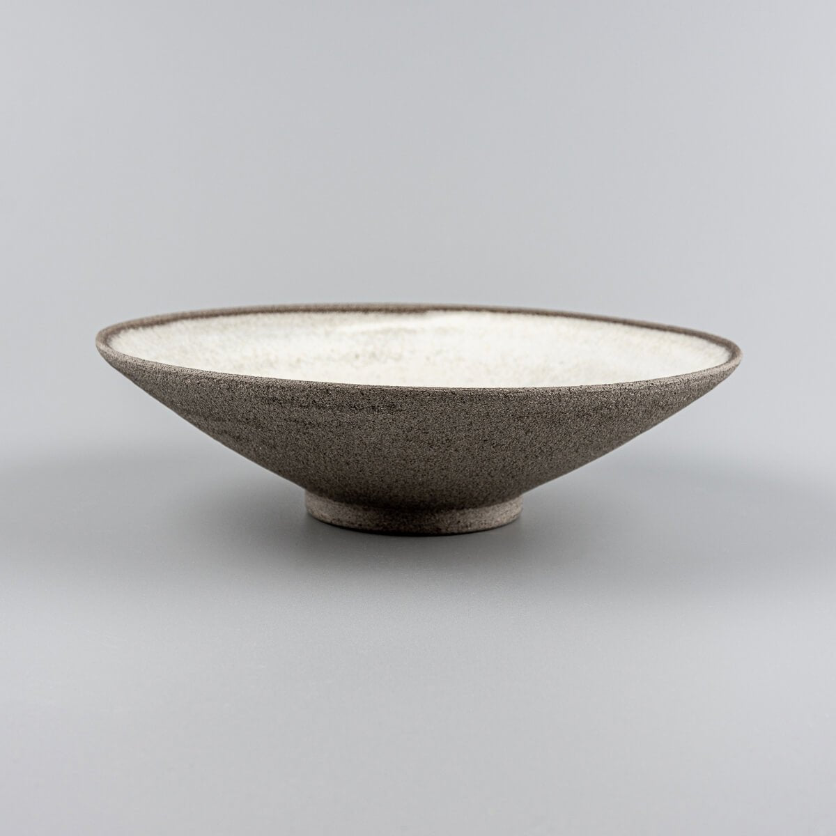 Profile view of modern ceramic plate with flared edges and dark stoneware exterior.