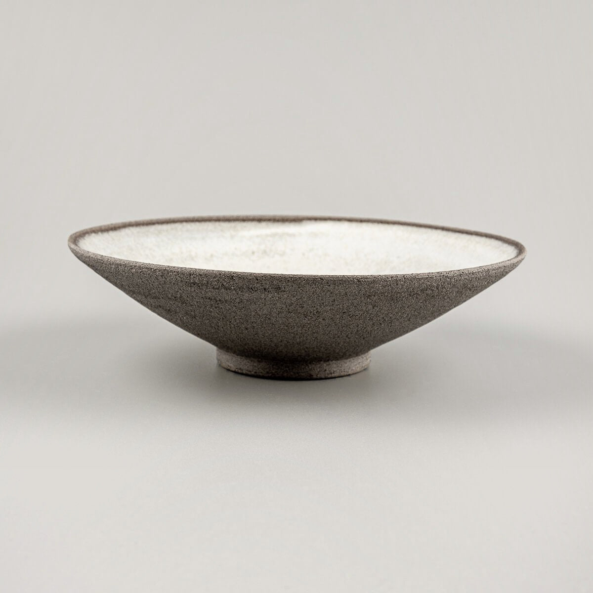 Profile view of modern ceramic plate with flared edges and dark stoneware exterior.