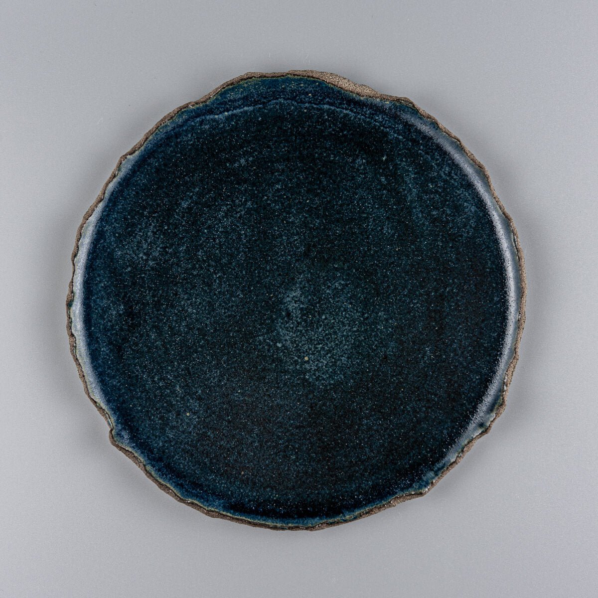 Flat handcrafted ceramic plate with matte blue glaze and textured raw edges, ideal for boutique hotel dessert service.