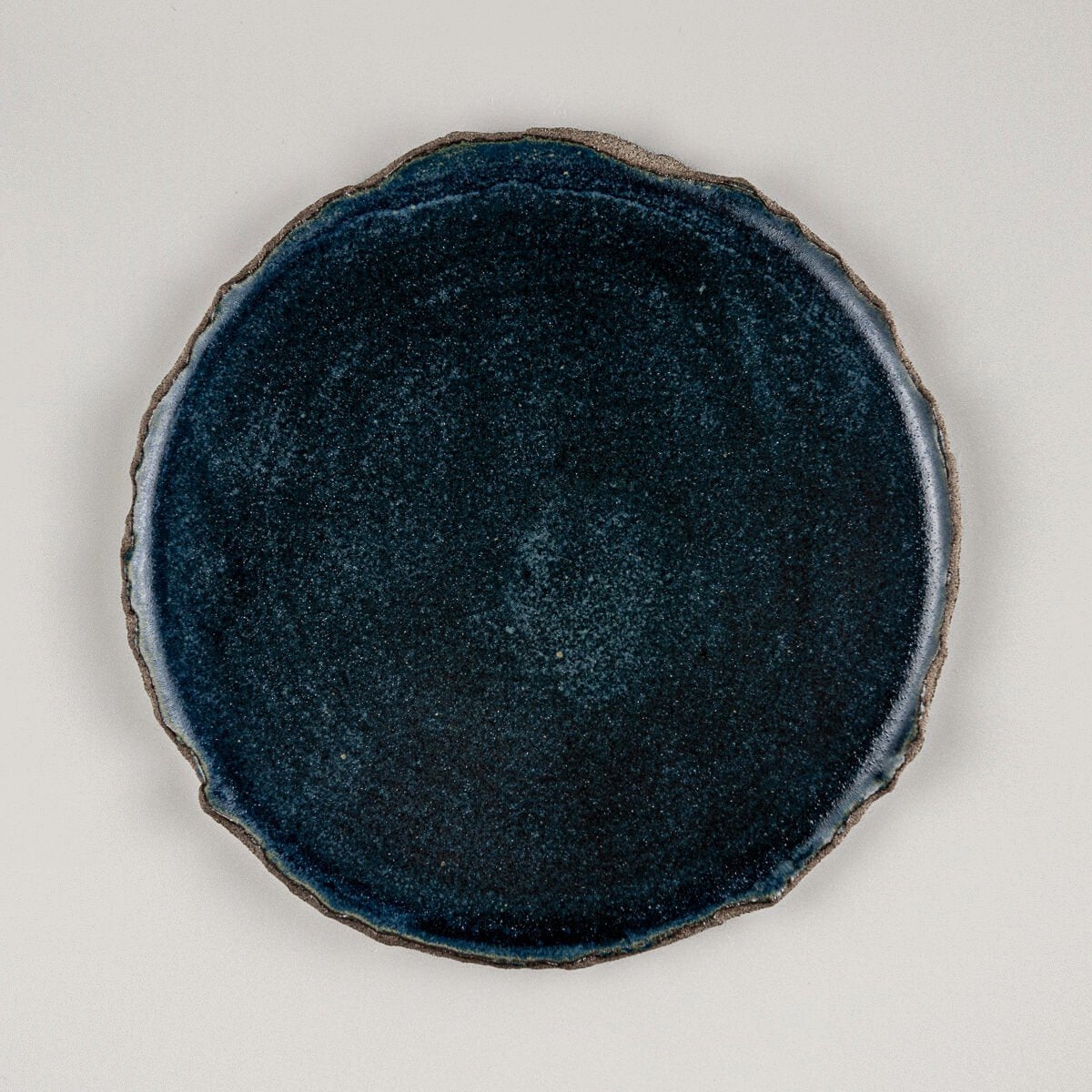 Flat handcrafted ceramic plate with matte blue glaze and textured raw edges, ideal for boutique hotel dessert service.