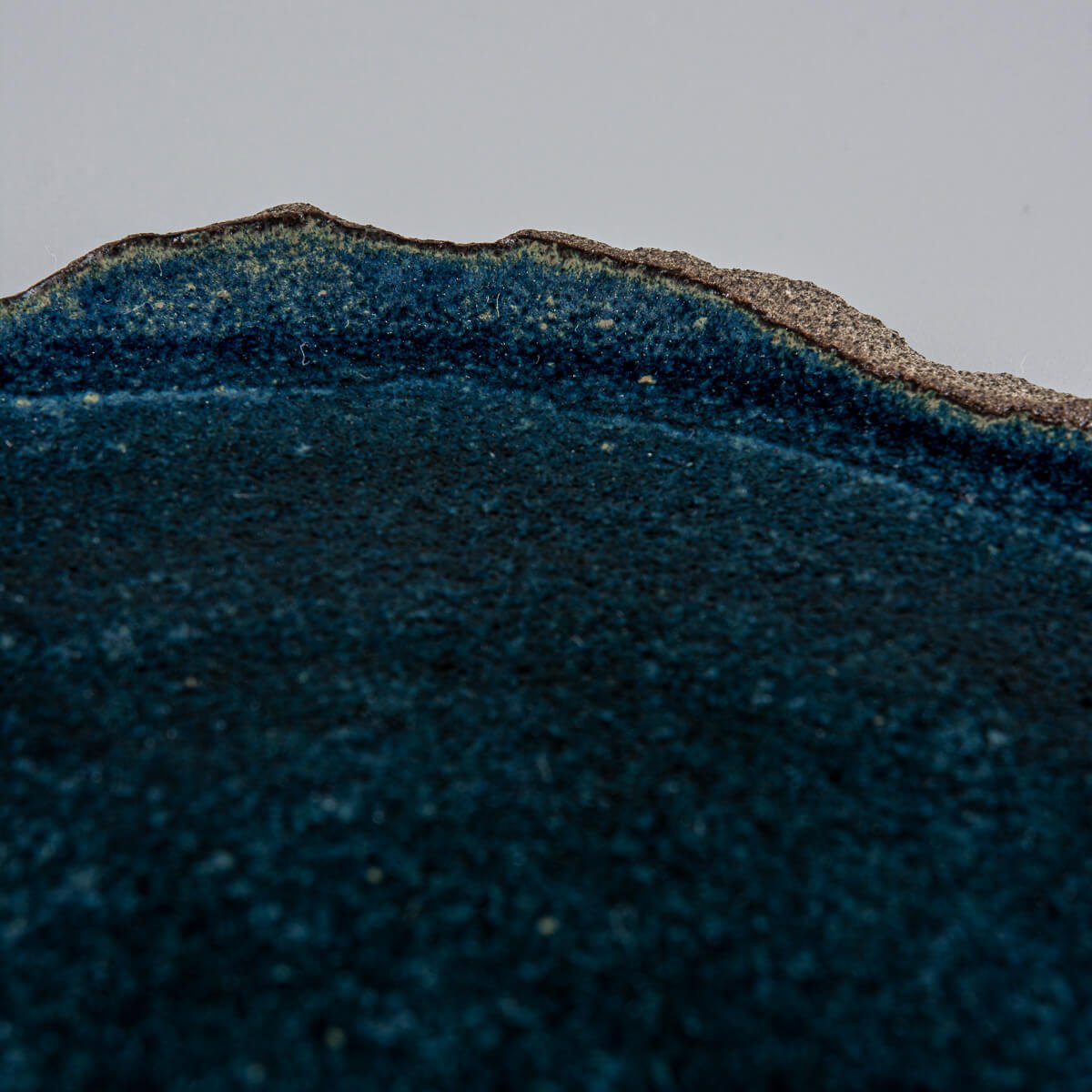 Detail of natural stoneware edge contrasting with matte blue glazed interior for a unique handmade look.