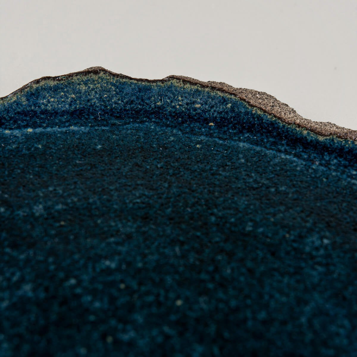 Detail of natural stoneware edge contrasting with matte blue glazed interior for a unique handmade look.