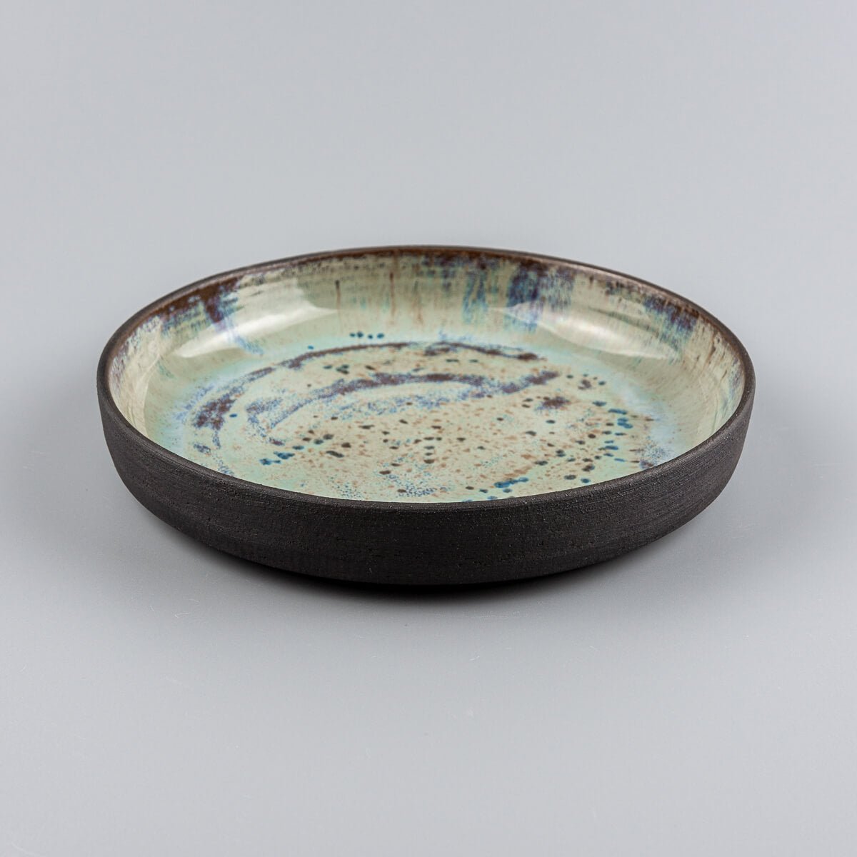 Side view of a handmade ceramic plate with raised edges and cosmic glaze detail.