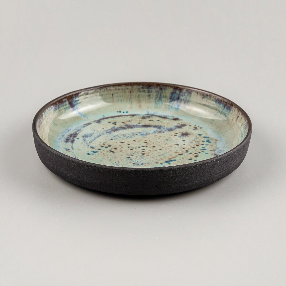 Side view of a handmade ceramic plate with raised edges and cosmic glaze detail.