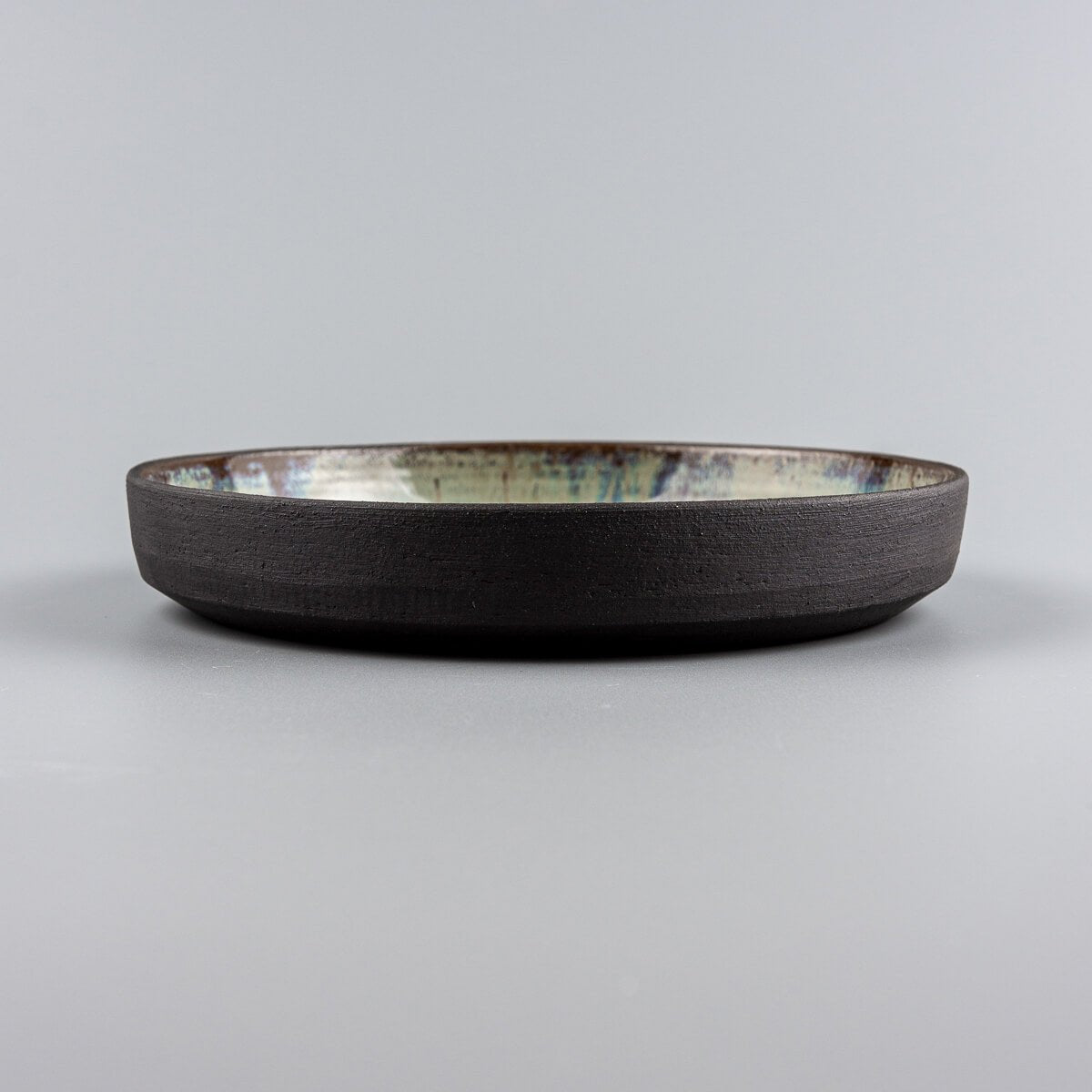 Profile shot of a dark stoneware ceramic plate with unique glazed interior.