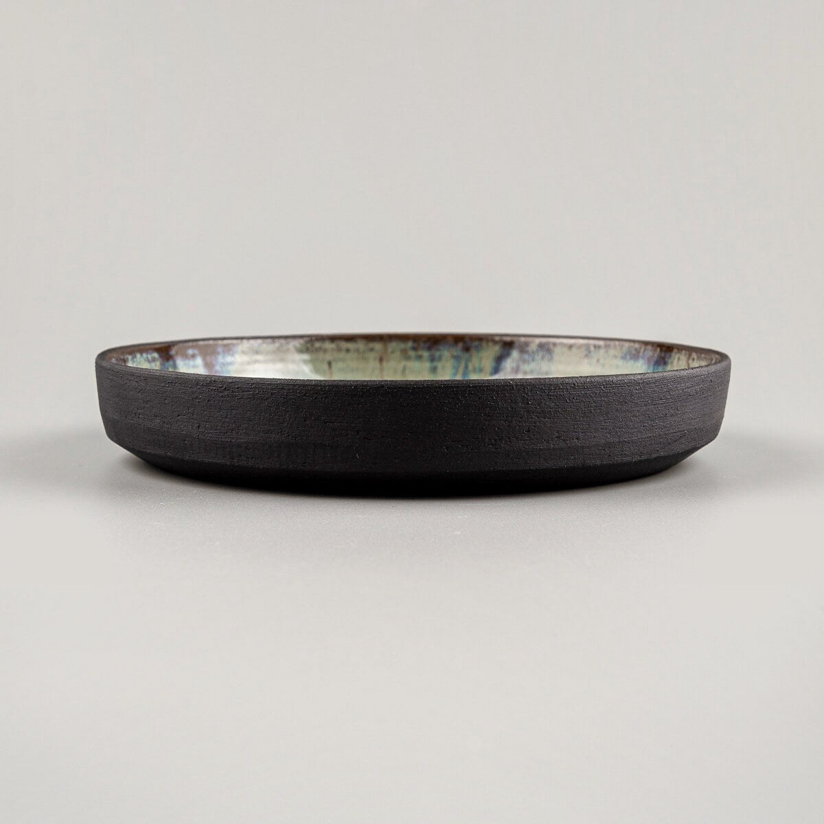 Profile shot of a dark stoneware ceramic plate with unique glazed interior.