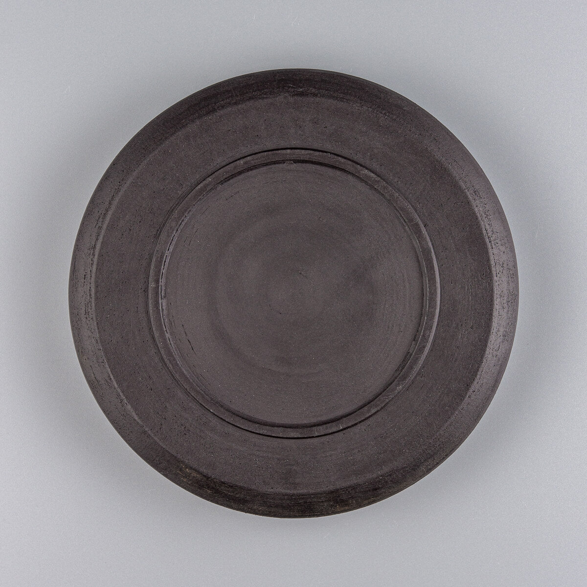 Bottom view of black stoneware plate showing raw ceramic base texture.