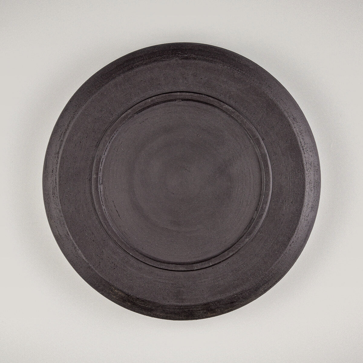 Bottom view of black stoneware plate showing raw ceramic base texture.