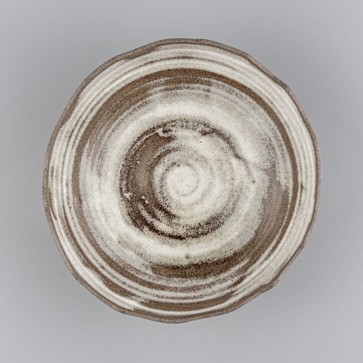 Top view of artisan stoneware bowl featuring swirling glaze pattern and handmade irregular rim.