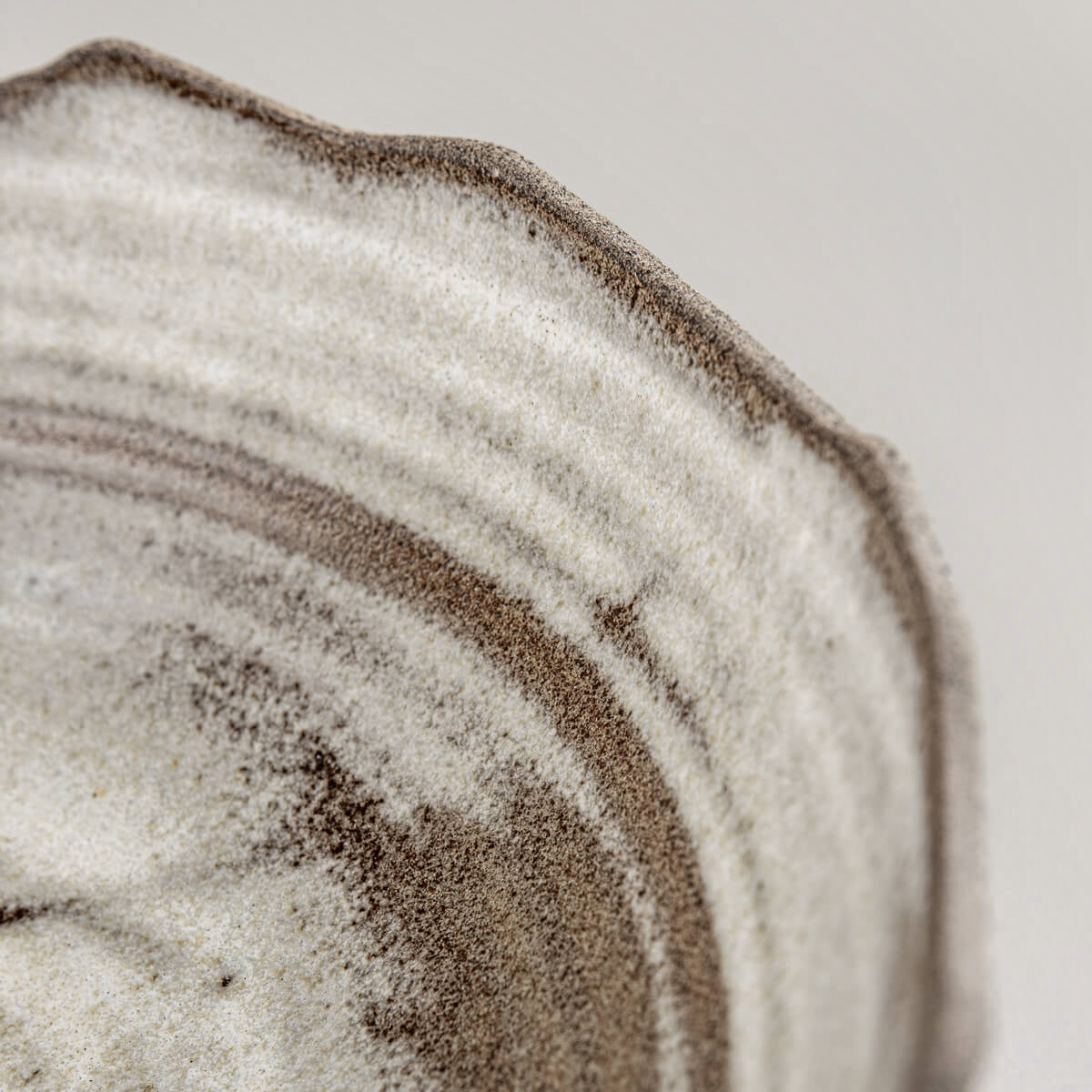 Detail view of uneven rim and layered glazing on artisanal ceramic serving bowl.
