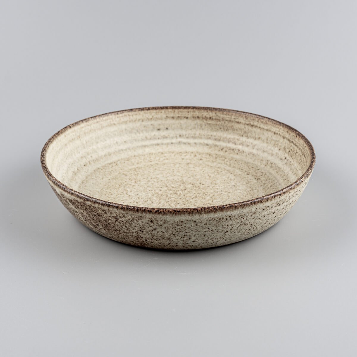 Side view of artisanal deep ceramic plate with rounded edges and earthy glaze tones.