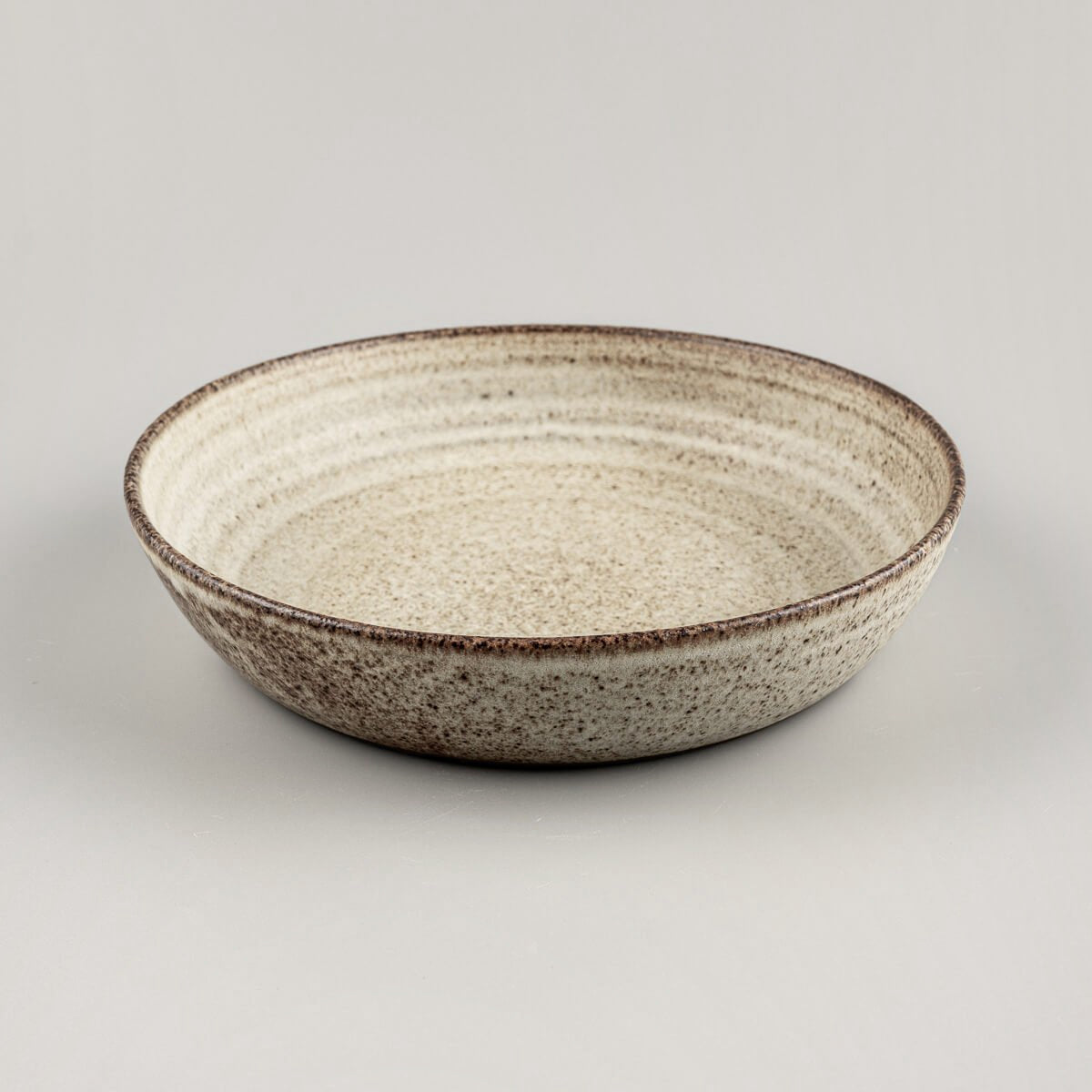 Side view of artisanal deep ceramic plate with rounded edges and earthy glaze tones.